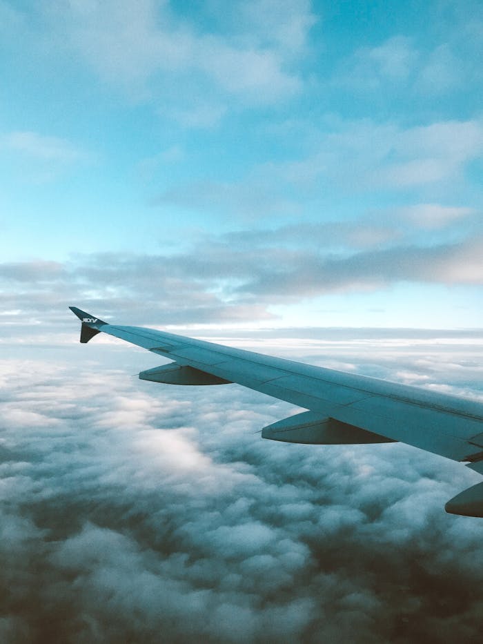 Aerial view of an airplane wing flying over fluffy clouds under a clear blue sky.