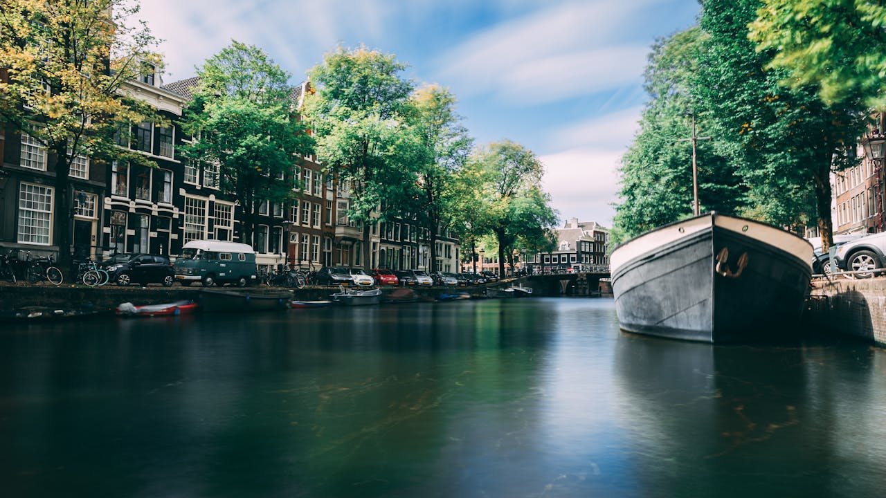 Peaceful Amsterdam canal scene with historic buildings and a moored boat under a clear sky.