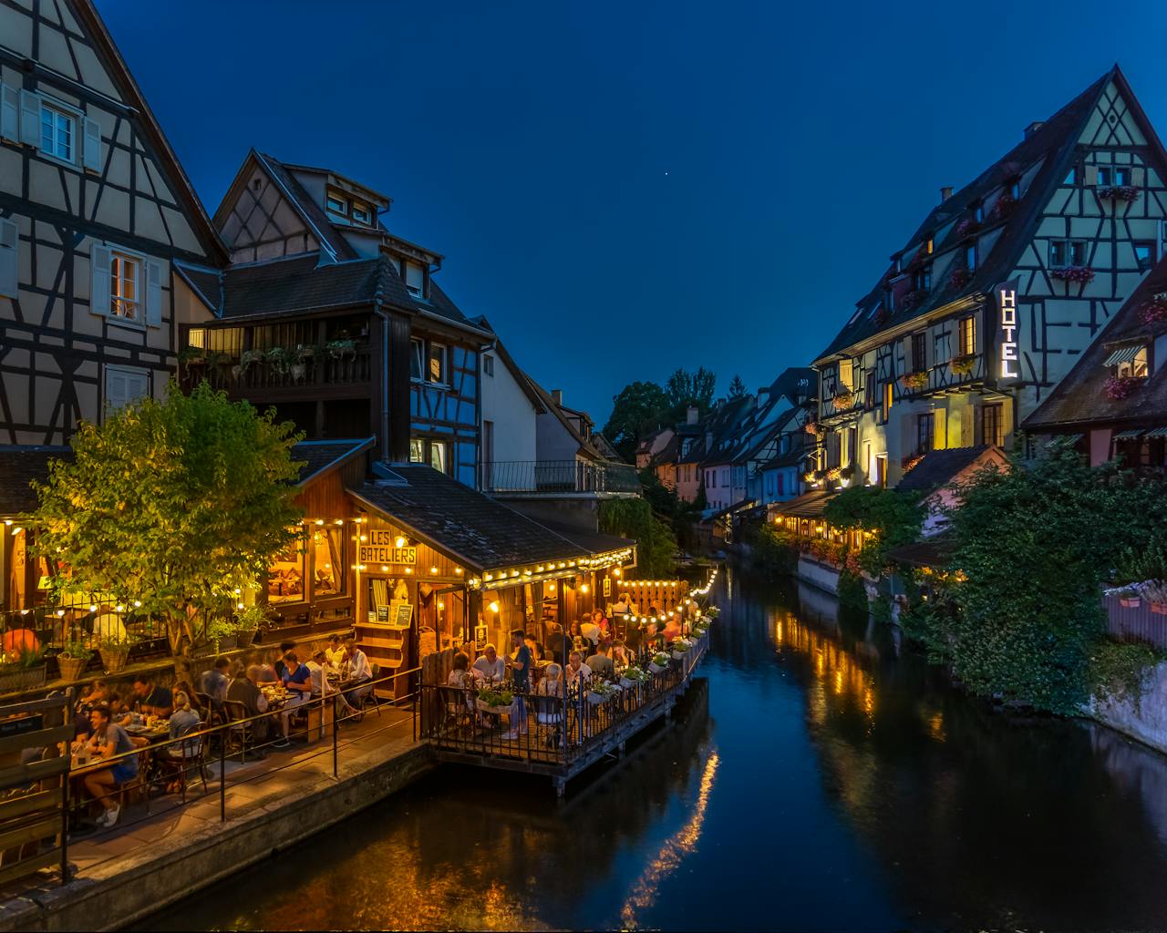 gallery-1 Nighttime view of Colmar's timbered houses and canal-side dining, beautifully illuminated.