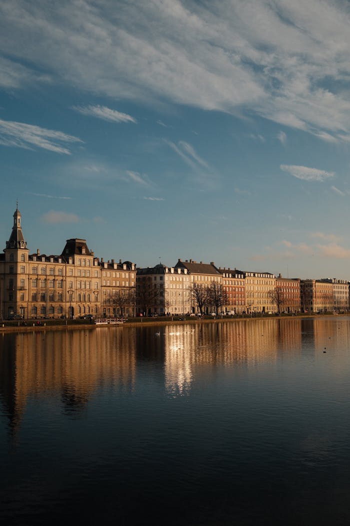 gallery-4 Serene cityscape reflecting on the river during sunset, showcasing historic buildings.